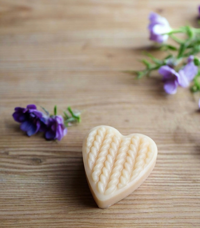 Heart-shaped soy wax melt on a wooden surface with purple flowers