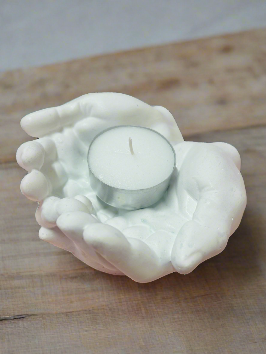 White ceramic hand-shaped holder with a candle on a wooden surface